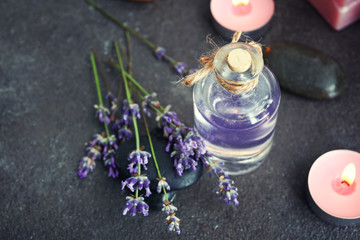 Obraz na płótnie Canvas Bottle of lavender essential oil and candles on grey table