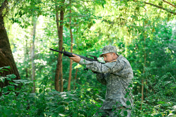 Soldier in camouflage taking aim in forest