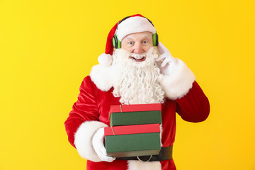 Portrait of Santa Claus with gift boxes listening to music on color background
