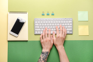 Female hands with PC keyboard, mobile phone and stationery on color background