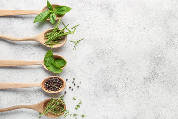 Spoons with different fresh herbs and spices on light background