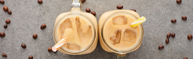 top view of ice coffee in glass jars with straws and coffee grains on grey background, panoramic shot