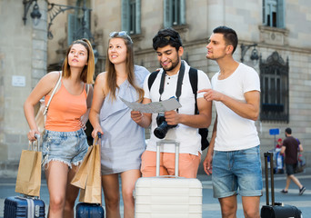 Fototapeta na wymiar four cheerful travelers holding map in hands and looking for their way in european town