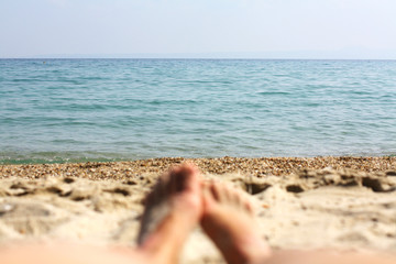 Fototapeta na wymiar Female feet, sandy beach and sea in the background. Picture with soft focus and place for your text. summer concept. Enjoying the sea or ocean. Focus is on the sea. Vacation holidays. Copy space.