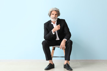 Fashionable senior man sitting on chair near color wall