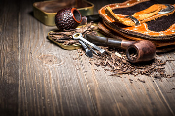 Wooden pipe with tobacco on wooden table. Tin boxes with tobacco, pipes and vintage background. Gentle man concept. Still life and prodoct photography.