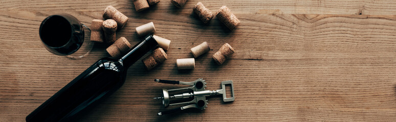 panoramic shot of bottle of wine, wine glass, corkscrew and corks on wooden surface