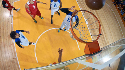 Professional basketball player in action performing slam dunk in a basketball hoop on a sports arena. View from above the hoop.