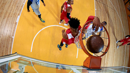 Professional basketball player in action performing slam dunk in a basketball hoop on a sports arena. View from above the hoop.