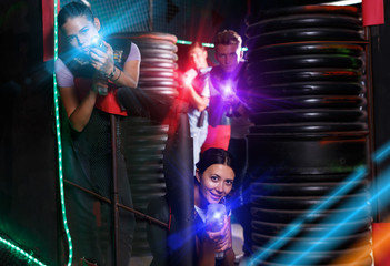 Naklejka na ściany i meble Friends playing laser tag game with laser guns together in dark