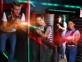 Young men and girl in waistcoats with laser guns playing laser t