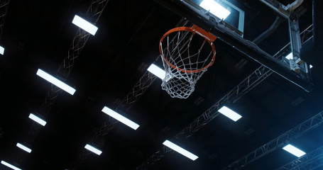 Low angle of professional basketball player in action performing slam dunk in a basketball hoop on a sports arena