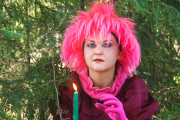 Young witch in purple clothes with a candle in his hand in the forest.