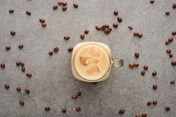 top view of delicious ice coffee in glass jar near coffee grains on grey background