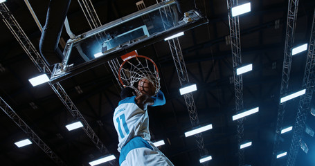 Low angle of professional basketball player in action performing slam dunk in a basketball hoop on a sports arena © haizon