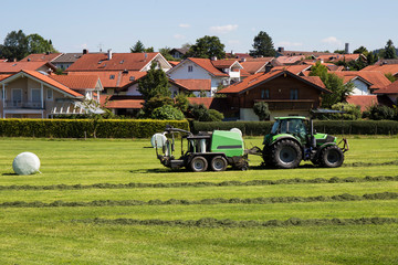 Agricultural landscape. harvester  wraps dry hay  in plastic white foil, summer in a Deutschland,Bavaria.