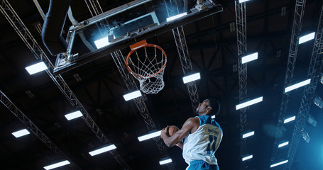 Low angle of professional basketball player in action performing slam dunk in a basketball hoop on...