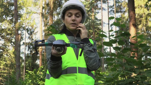Woman Worker talking on phone and holding Drone Quadcopter in forest