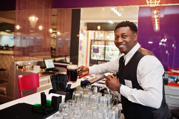African american bartender at bar hold fresh dark beer at glass in pub.