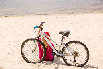 Back view of young slim woman standing at bicycle on stony sidewalk under clear blue sky background. Active lifestyle and vacations concept.