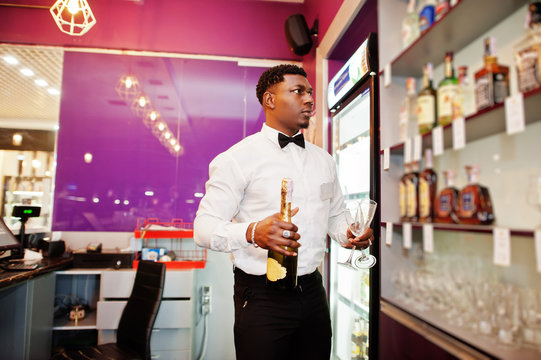 African american bartender at bar holding champagne with glasses.