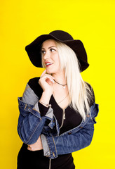 beautiful blonde girl in a hat and a denim jacket is smiling on a yellow background