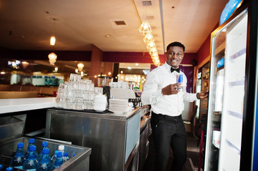 African american bartender at bar taking energy drink from fridge.