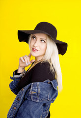 beautiful blonde girl in a hat and a denim jacket is smiling on a yellow background