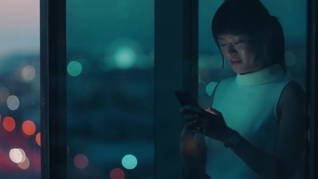 asian business woman using smartphone texting looking out window corporate executive sending emails on mobile phone working late managing company