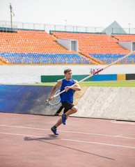 Pole vault - a young man runs up holding a pole in stadium