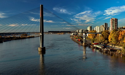 Fototapeta premium New Westminster City the slopes of the Fraser River, painted with autumn colors, Sky Train Bridge and a road against the background of a bright sky with white clouds