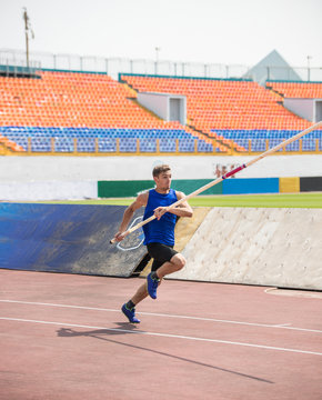 Pole vault - a young man runs up holding a pole in stadium
