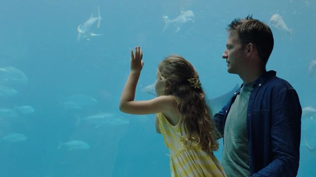 father with little girl at aquarium taking photos of fish using smartphone enjoying marine life swimming in tank having fun at oceanarium sharing on social media