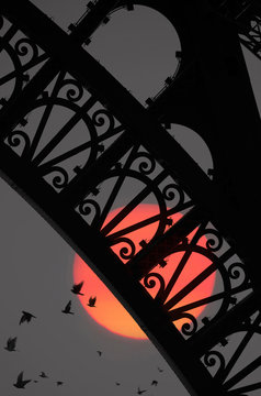 Close up of arch of Eiffel Tower with moon and flock of birds in background
