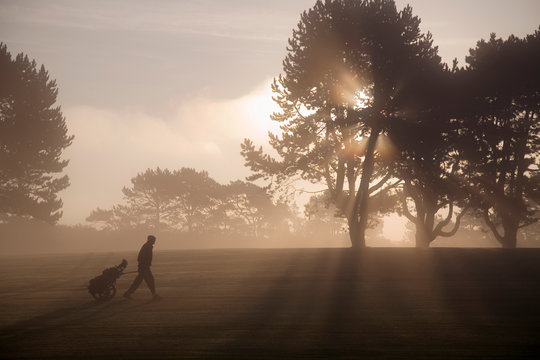 Side view of man with golf trolley walking on golf course