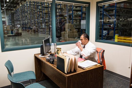 Man drinking coffee while sitting in office at distribution warehouse