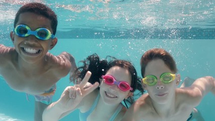 happy children swimming underwater in pool smiling waving hands children enjoying swim floating together in crystal clear water on summer vacation - Powered by Adobe