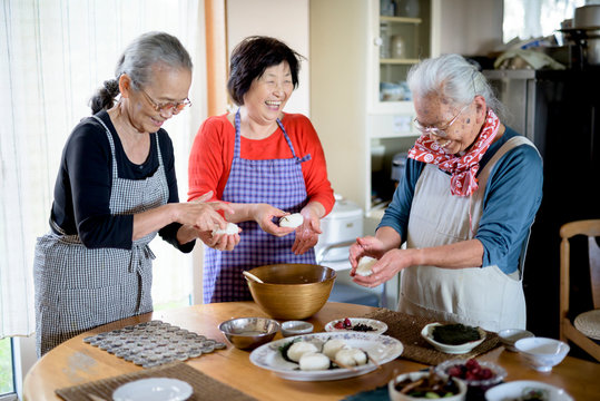 Women preparing sushi while standing at table in kitchen