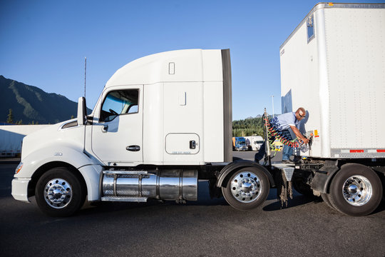 Man attaching power cable from truck tractor to trailer at truck stop