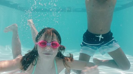 happy children swimming underwater in pool smiling waving hands kids enjoying swim floating together in crystal clear water on summer vacation