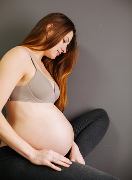 pregnant woman with nacked belly sitting om a bad in the room, grey background