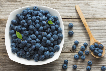 Appetizing fresh blueberries in white ceramic bowl with wooden background