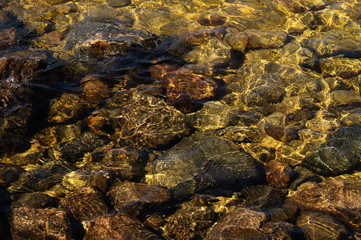 Shiny transparent water. clear water with pebbles and stone on the bottom. shining reflections of sun rays and ripples on the water