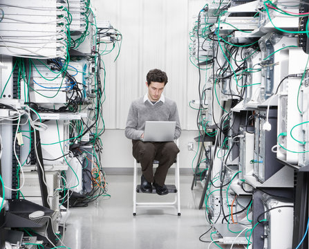 Technician working on laptop in computer server room