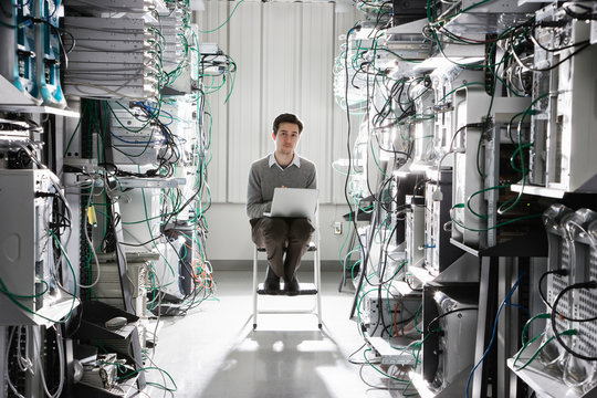 Portrait of technician working on laptop in computer server room