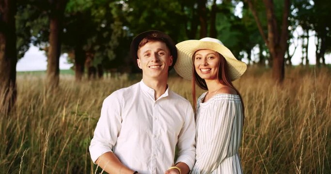 Joyful young man and lady in white outerwear and hats enjoying time on nature, looking in camera and smiling, portrait