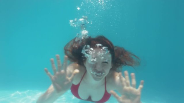 beautiful woman swimming underwater in pool smiling waving hand floating in blue crystal clear water having fun swim in summertime 4k