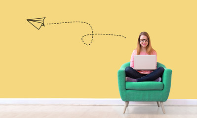 Paper airplane with young woman using her laptop in a chair
