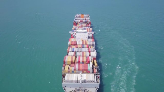 Aerial footage of a large container ship at sea, loaded with various container brands