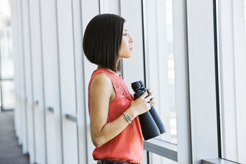 Side view of businesswoman with binocular looking through window